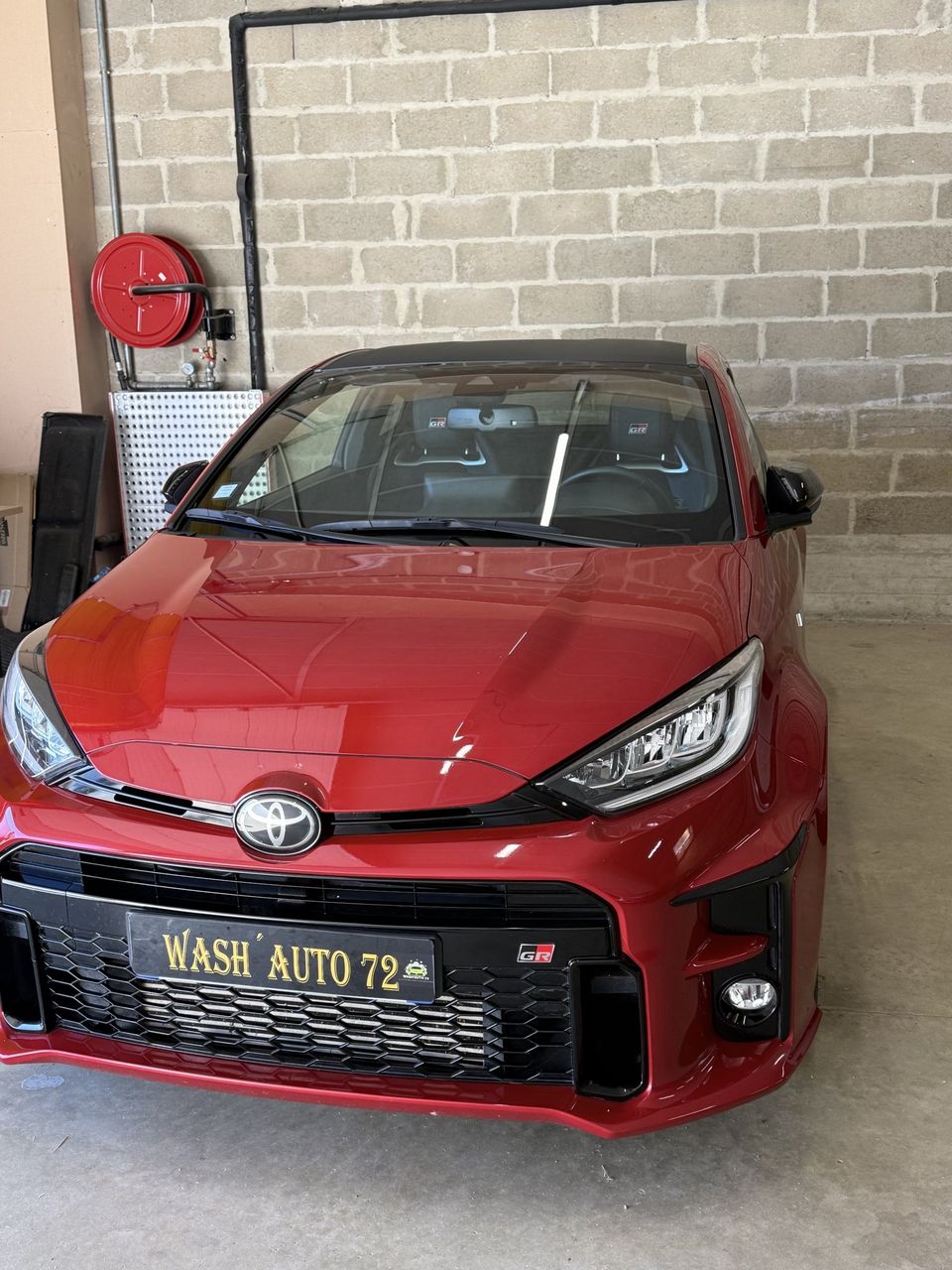 Toyota GR Yaris rouge nettoyée par Wash'Auto 72 dans un garage, plaque Wash Auto 72